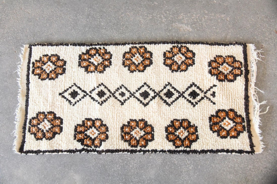 Moroccan Wool Shag Rug, Cream & Brown Flowers: Moroccan Wool Shag Rug, Cream & Brown Flowers. A sag rug with cream ground, central black diamond shapes, and brown & black flower border. Made of wool with a thick, plush pile. Dimensions are 40 in l