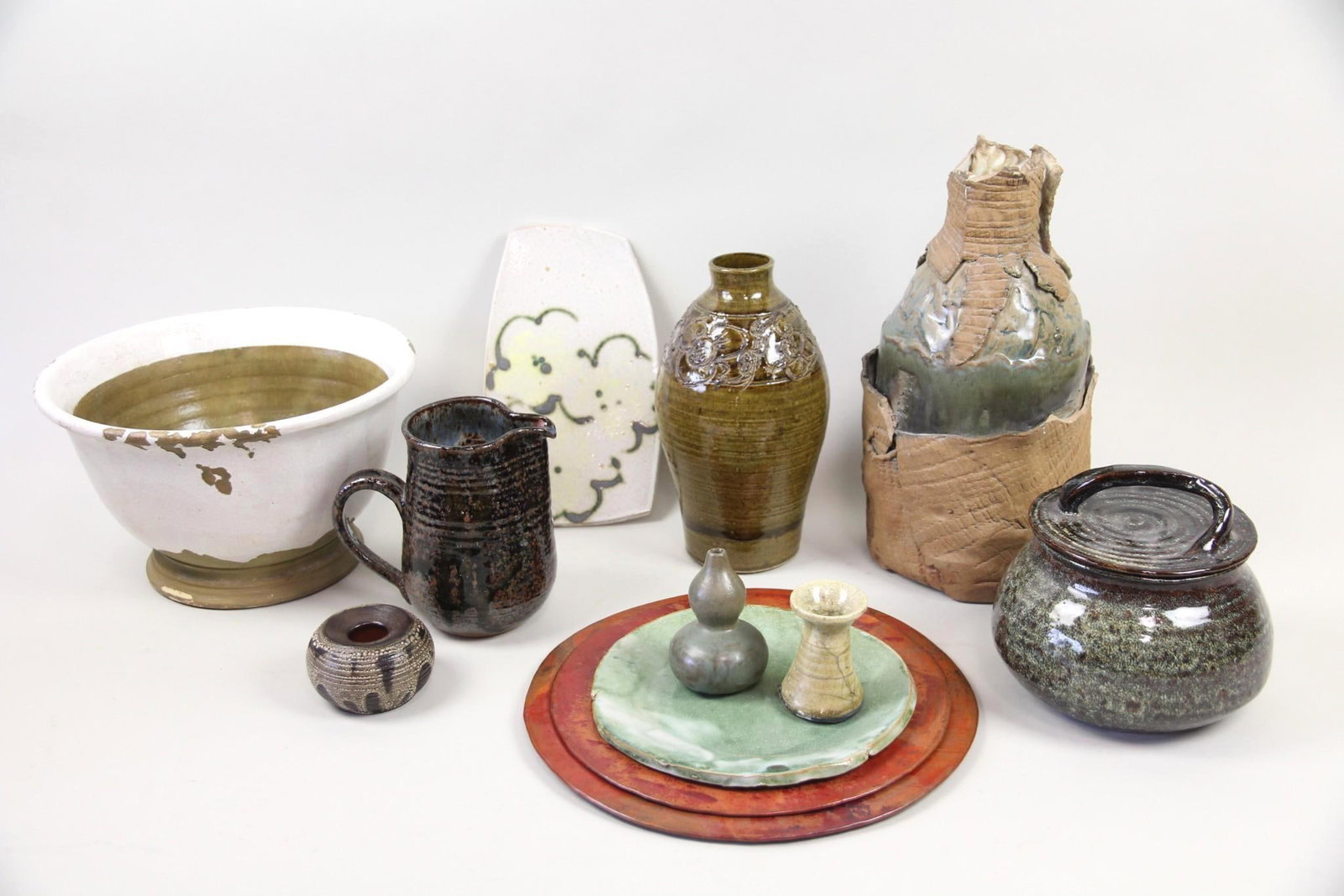 Lot of 10 Studio Pottery Vessels & 2 Metal Platters, Earth Tones: Lot of 10 Studio Pottery Vessels & 2 Metal Platters, Earth Tones. Group of studio made pottery in neutral & earthy glazes, including 5 vases, 2 plates, a pitcher, a jar, and a bowl. Also included are 