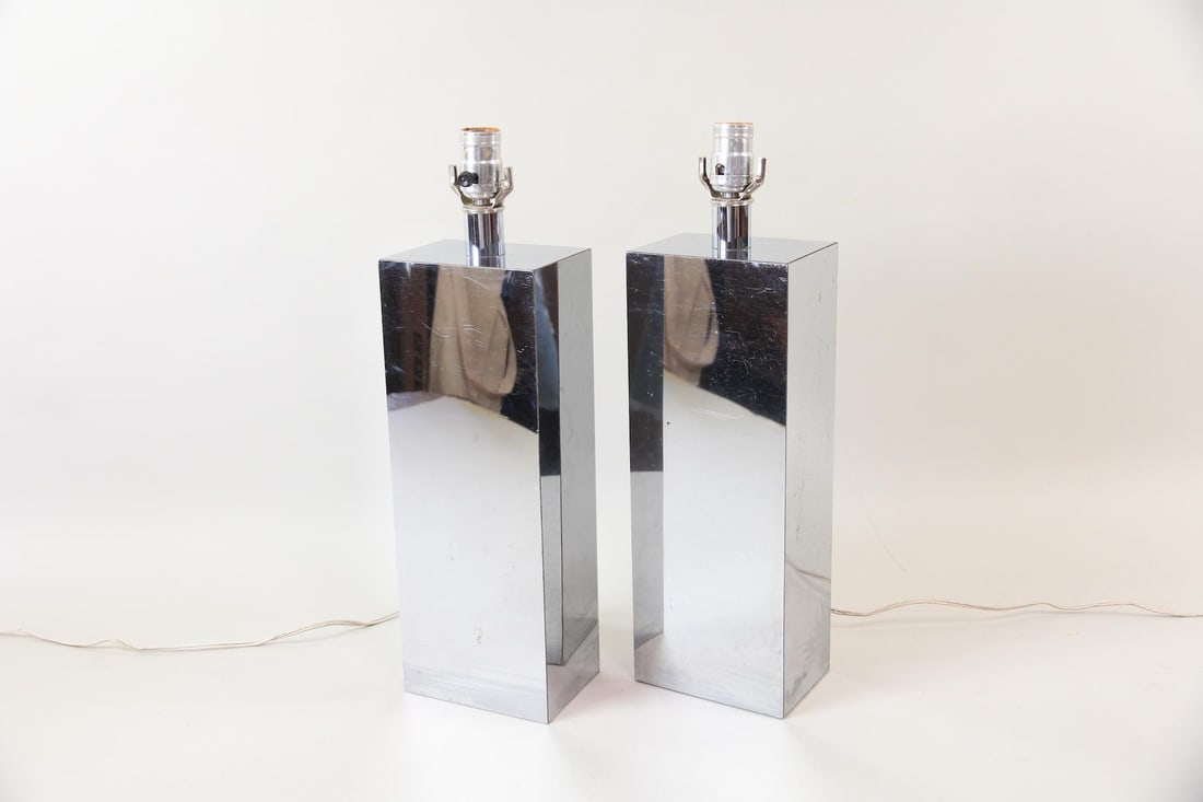 Pair of Modernist Mirrored Chrome Table Lamps: Pair of Sculptural Mirrored Minialist Chrome Table Lamps. A pair of lamps with tall bases and mirrored chrome finish. Dimensions are 19 in h x 5.5 in w x 4 in d. Condition is good with minor scuffs