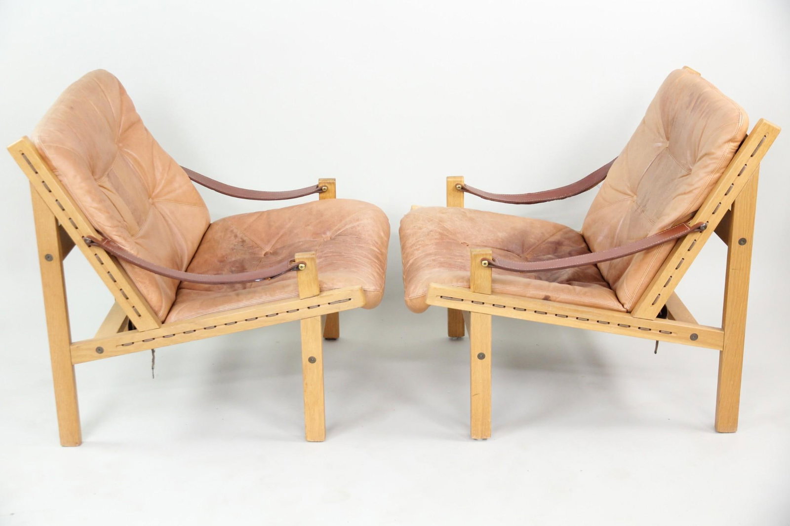 Pair of Leather "Hunter" Chairs by Torbjorn Afdal: Pair of Scandinavian Modern Torbjorn Afdal "Hunter" Leather Lounge Chairs. Matching chairs with wooden frames and sling arms, featuring light brown leather cushions and exposed stitching to the edges.