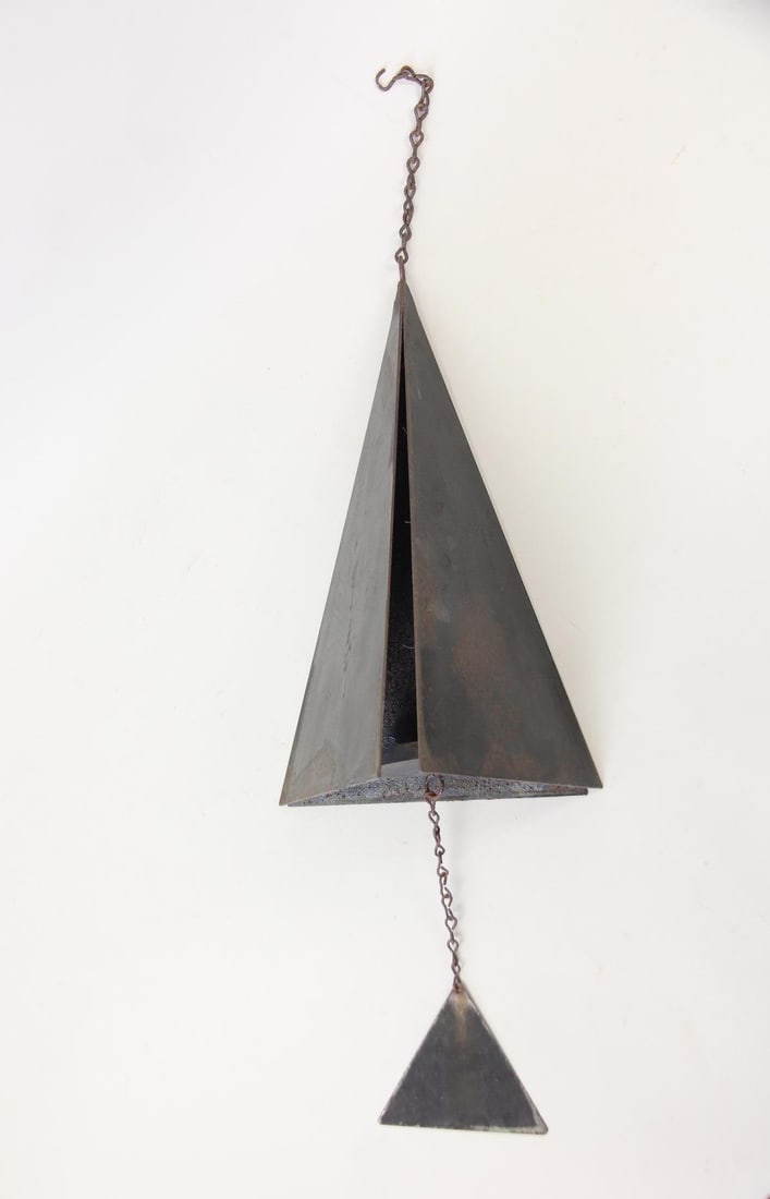 Minimalist Pyramid Iron Wind Chime: Mid-Century Modern Pyramid Iron Wind Chime. This chime features a large, hollow pyramid-shaped bell with a smaller pyramid clapper hanging from a chain below. It has a weathered surface. Dimensions