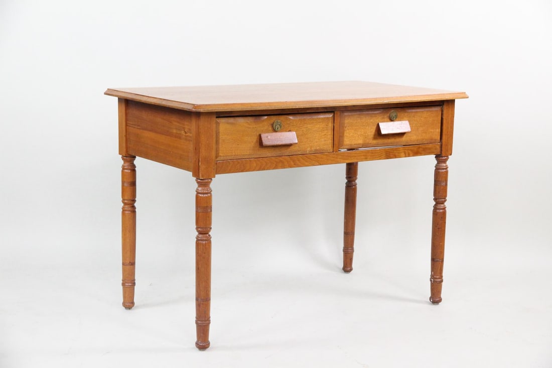 Wooden Writing Table, Oberlin College: Wooden 2-Drawer Desk, Oberlin College. A desk made of warm-toned wood with two drawers, block handles, and turned legs. Stamped Oberlin College to the underside. Dimensions are 29.25 in h x 42.25 in w