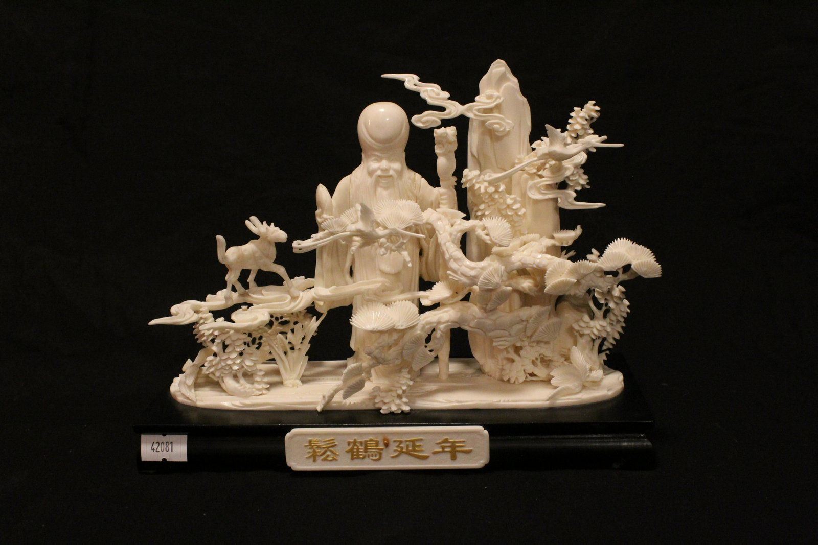 Intricately Carved Bone "Longevity": Intricately Carved Bone "Longevity". Depicting a bearded man draped in robes in nature, various wildlife among the foliage and rocks. On lacquered wood base with painted character bone plate. From Pri