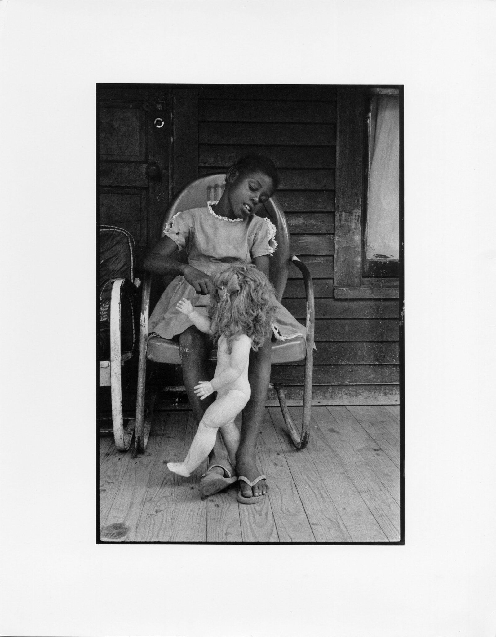 BRUCE DAVIDSON Child on a Front Porch Playing, 1962: BRUCE DAVIDSON (1933-), CHILD ON A FRONT PORCH PLAYING WITH HER DOLL BABY, SHELBY COUNTY, TN, 1962 gelatin silver print, printed later; 10 x 6 11/16 (image), 11 x 14 in. (sheet); Magnum label affixed