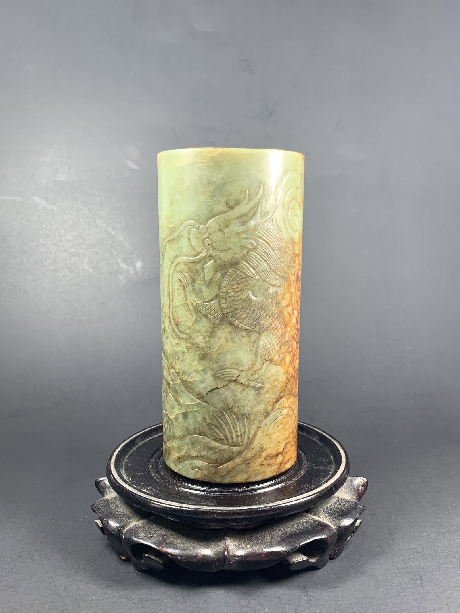 A Chinese Dragon Carved Jade Opium Pipe Holder: A Carved Green & Russet Jade Tube Form Opium Piper/ Incense holder with relief carvings of A large Dragon appearing from amongst the clouds and mountain tops in pursuit of a pearl of wisdom with a dog