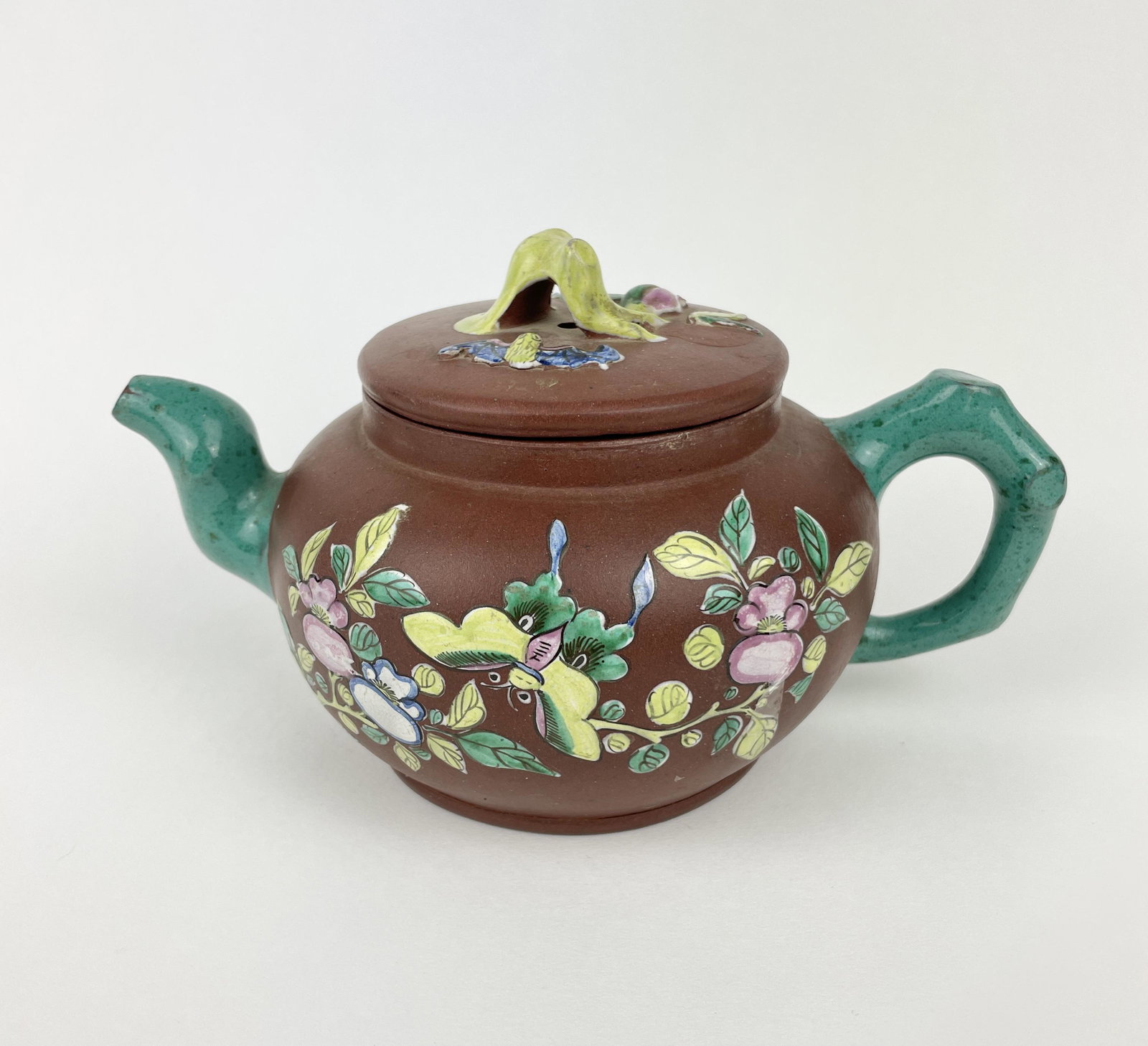 A Chinese 19th Century Yixing Teapot: A Chinese 19th Century Yixing Teapot of medium brown tone with Turquoise enameled handle and spout, the lid of the teapot featuring relief applied enamel handle of root form, peach and Bat. The body o