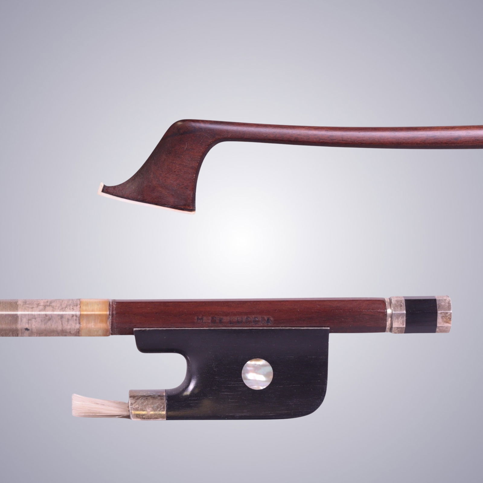 A CELLO BOW STAMPED M. DE LUCCIA: A CELLO BOW STAMPED M. DE LUCCIA Of Round Stick, Ebony & Silver mounted. Stamped on stick above frog: M. DE LUCCIA Approximate Dimensions: 71.8 cm (Total Length - Head to Adjustor) 73.6 Grams in