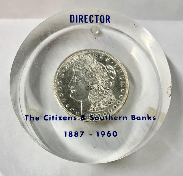 1921 Morgan Coin Paperweight: 1921 Morgan Coin Paperweight Set in Acrylic. Marked: DIRECTOR The Citizens & Southern Banks 1887-1960. There are a few nicks and scratches in the acrylic. Apx. 3" diameter and 1"h. Photos are consider