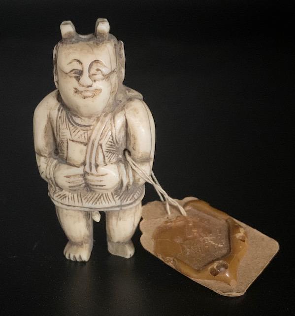 Asian Netsuke with Wax Stamp Arm Tag: Asian Netsuke with Wax Stamp Arm Tag. Standing Man with Short Robe With Moveable Penis. Hand Carved Iv0ry? Apx. 2" H. There is damage on one foot as pictured. Photo's are considered part of the descri