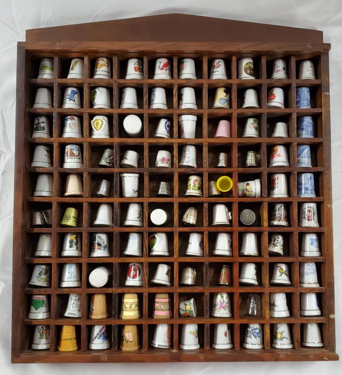 Collection of 101 Thimbles in Display Cabinet: Collection of 101 Thimbles in Display Cabinet. Assortment of Porcelain, Pewter, Wood, Metal, Plastic, & Glass Thimbles. Some Souvenir and Advertising. Plastic front on Cabinet is yellowed as pictured.