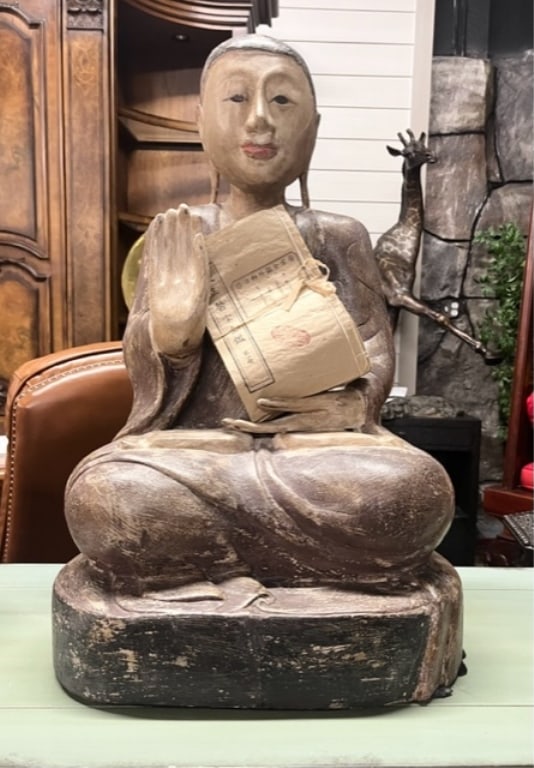24" Carved Wood Sitting Buddha: 24" Carved wood buddha. Stack of asian papers in hand. Approx. 24"H x 14"W. Photos are considered part of the description and condition.