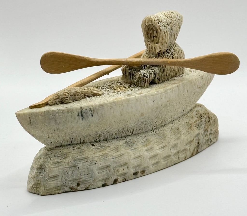 Fossilized Bone Carved Inuit in Kayak: Fossilized bone carved Inuit in kayak. Approx. 6"L. Photos are considered part of the description and condition. G-G11