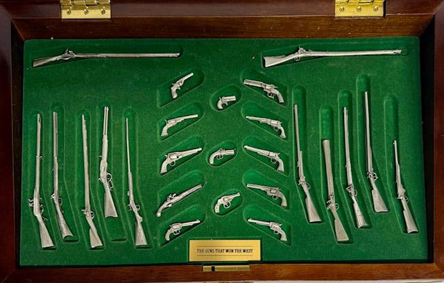 Franklin Mint "The Guns That Won The West": Franklin Mint "The Guns That Won The West" replica gun collection. Includes 25 miniature pewter replica guns in a mahogany display case with green felt interior. Scuff present on acrylic. Produced in