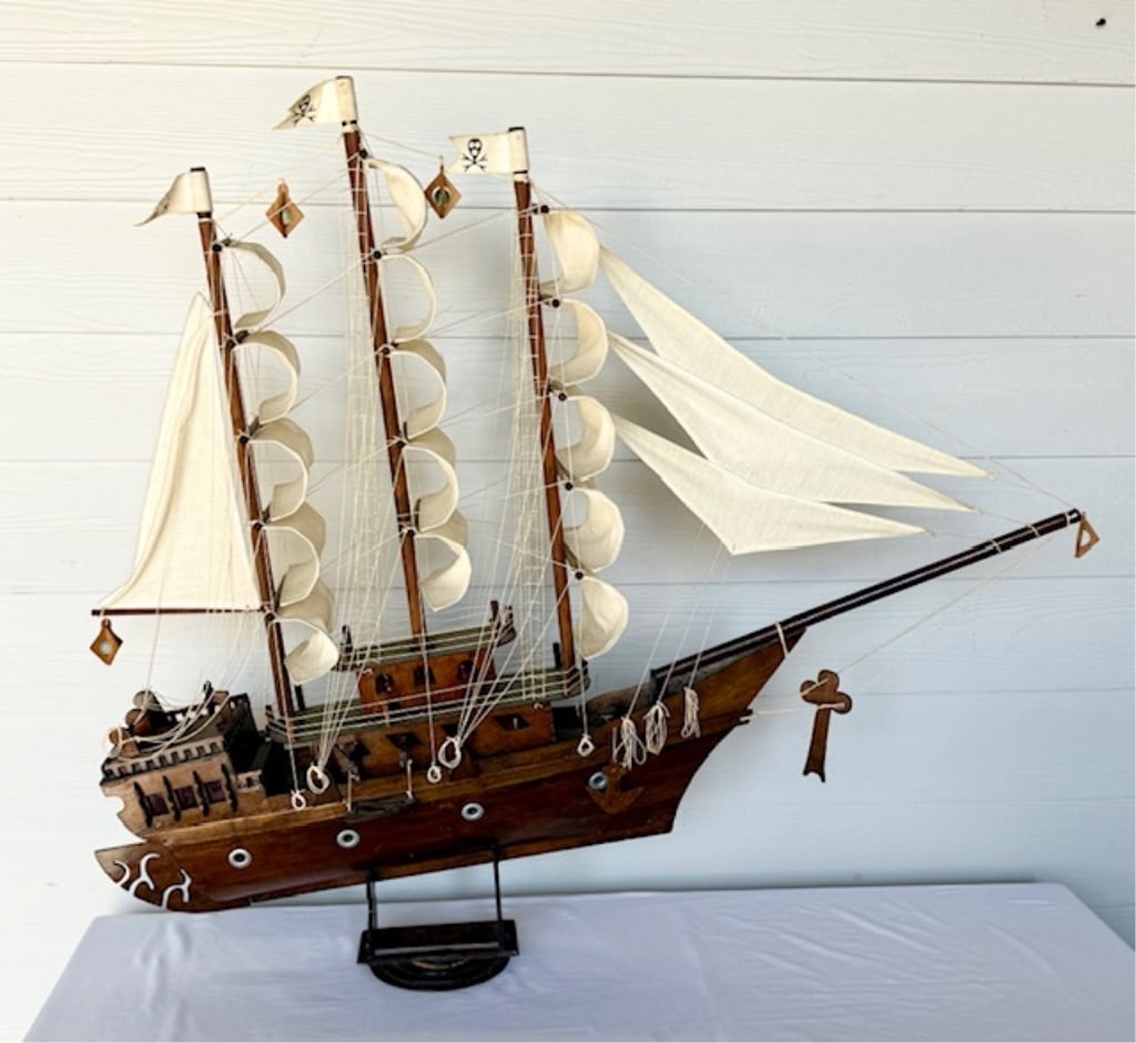 Vintage Wooden Model Pirate Ship: Vintage wooden model pirate ship. Hand crafted wood body with cloth sails. Some stains present on sails. Features 3 flags with skull and cross bones and red cellophane windows. Wood frame accents with