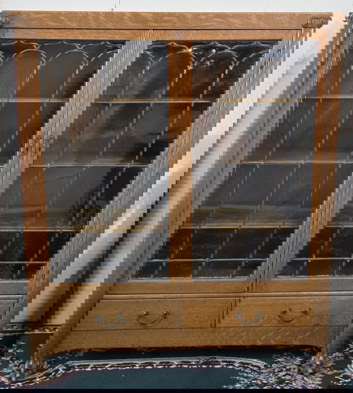 Vintage Double Door Glass Front Cabinet: Vintage double door oak cabinet. Features leaded glass doors and two lower pull drawers. 3 Wooden shelves. Paw feet. Chip present on one foot. In good condition for age. Approximately 55.5"h x