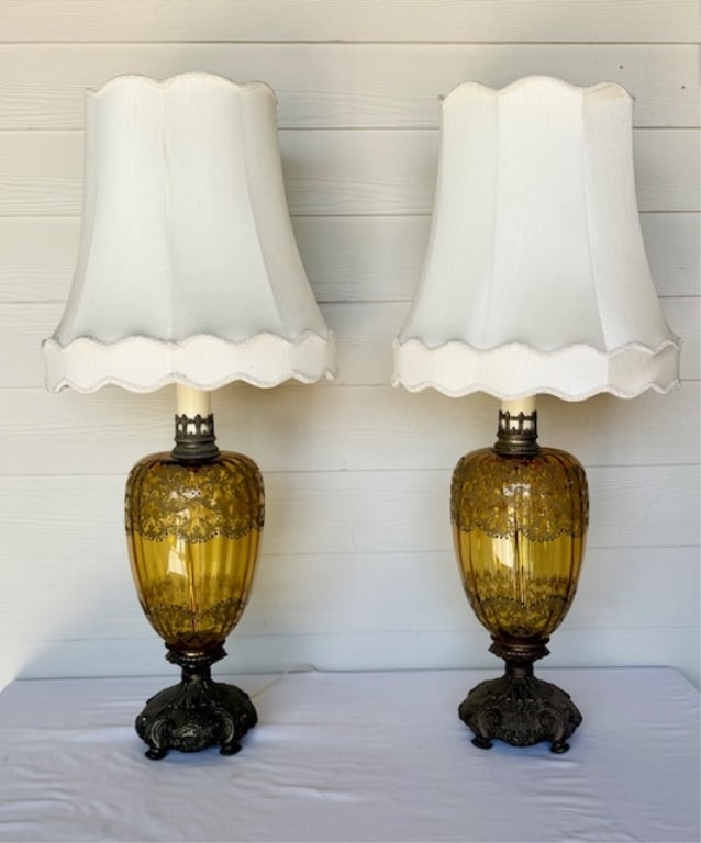 Pair Vintage MCM Amber Glass Table Lamps: Pair of vintage mid century modern amber glass table lamps. Both lamps feature applied paint? details on amber glass bodies and heavy metal bases. Single bulb. White fabric shades. Rip present on insi