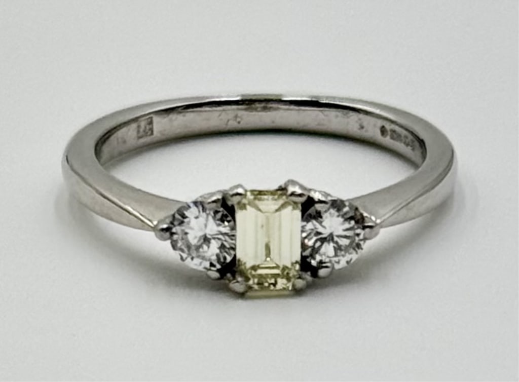 Platinum Fancy Yellow Diamond Ring - 3.76g TW: Lovely platinum fancy yellow diamond ring. Ring features center emerald cut .33 carat fancy yellow diamond with round clear diamond on each side. Marked on inside, C & M. Approximately size 6 and 3.76