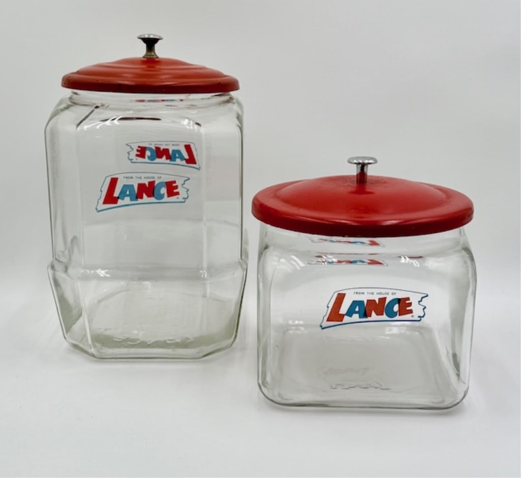 Pair of Vintage Glass Lance Cracker Jars: Pair of vintage glass Lance Crackers jars. Both feature clear glass bodies with the iconic red metal lids. Lids are in good aged condition with some rust and wear. Includes 12" and 8" jar. Photos are