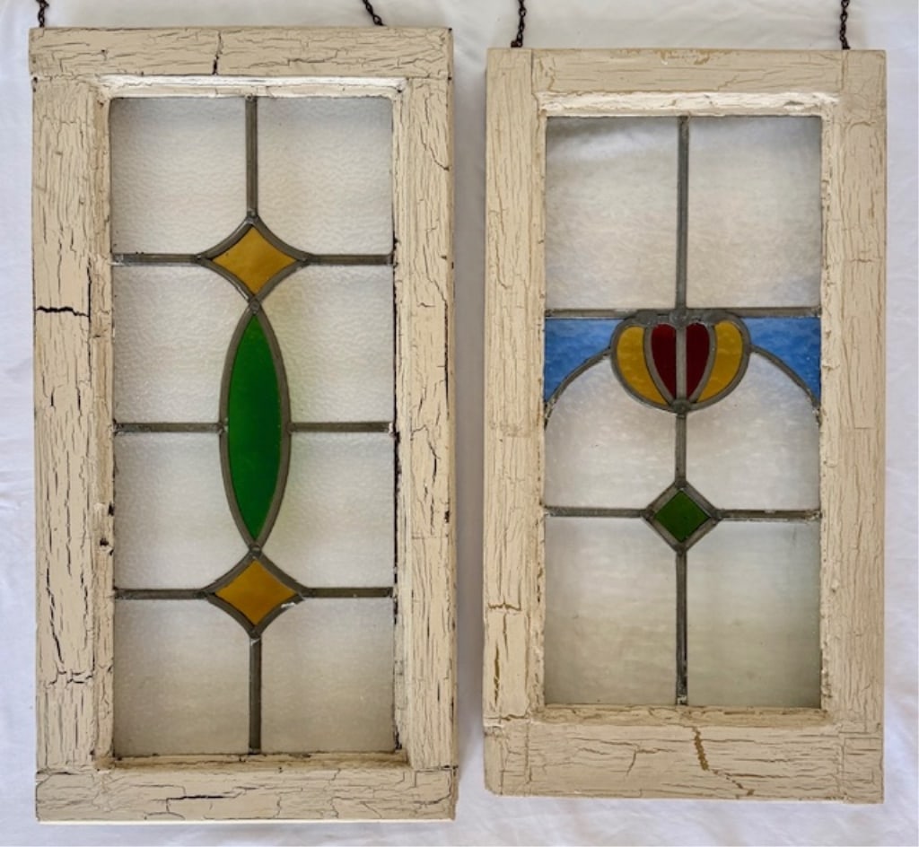 Pair of Antique Leaded Stained Glass Windows: Pair of antique leaded stained glass windows. Both windows feature vibrant red, yellow, green, and blue glass accents set within distressed white painted wooden frames. Top eye hooks for hanging. Appr