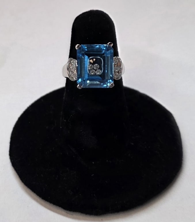 14K Blue Topaz Floating Diamond Ring - 5.84g: 14K White gold blue topaz floating diamond ring. The prong set center topaz contains four floating diamond with six additional diamonds accenting the recessed, banded shoulders. Band marked SBT.