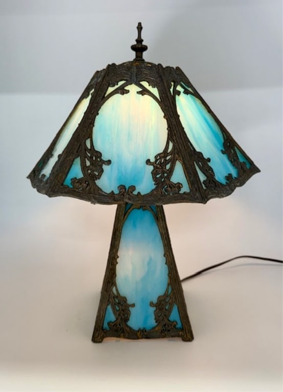 Antique Blue Slag Glass Table Lamp: Antique blue slag glass table lamp. Features blue slag glass panels with intricate floral swag framing on both the hexagonal shade and the base. Dual lite, top and bottom. Frame in aged condition