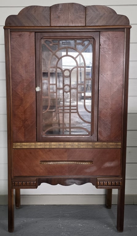 Antique Jacobean Style Waterfall Cabinet: Antique Jacobean Style waterfall cabinet. The central door features an intricate decorative wood overlay design over the glass. Single drawer has faux inlay. In good condition for age with some