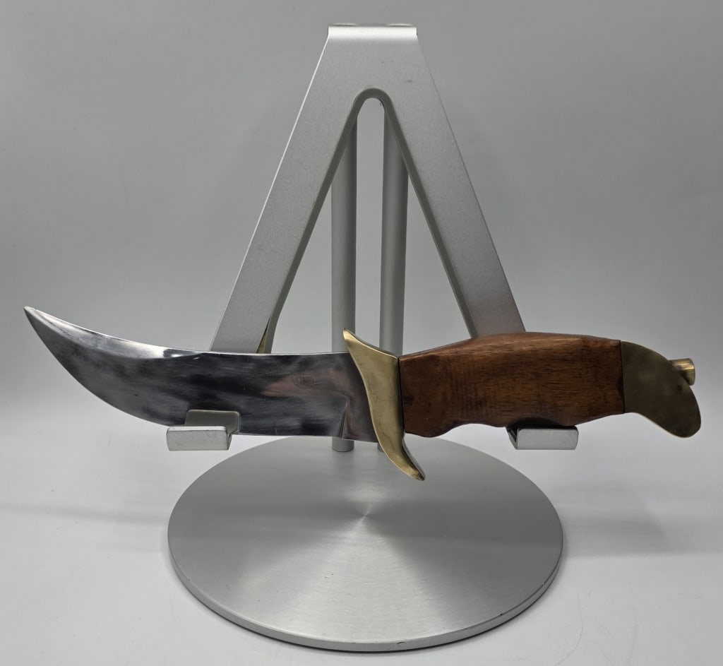 Vintage CVA Italy Fixed Blade Bowie Knife: Vintage CVA Italy fixed blade bowie knife. Features a stylized upswept bowie style blade, brass guard hilt, and pommel with a contoured wooden handle. On a display stand. Knife approximately 10"long.