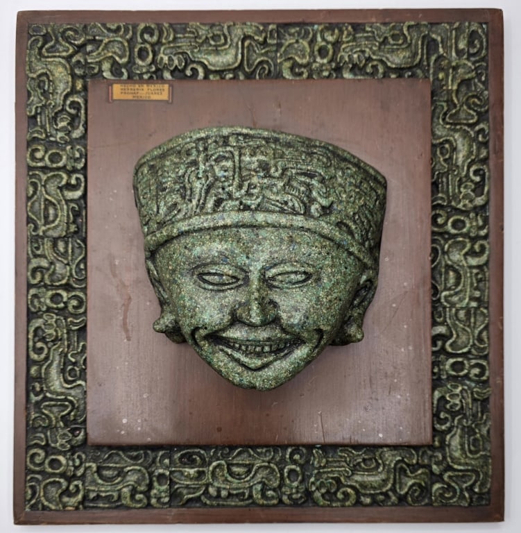 "Smiling Head" Crushed Malachite Stone Plaque: "Smiling Head" crushed malachite stone plaque. Mounted on a wooden base and surrounded by an intricately carved border featuring Aztec inspired motifs. Approximately 11.5"h x 11"w. Photos are consider