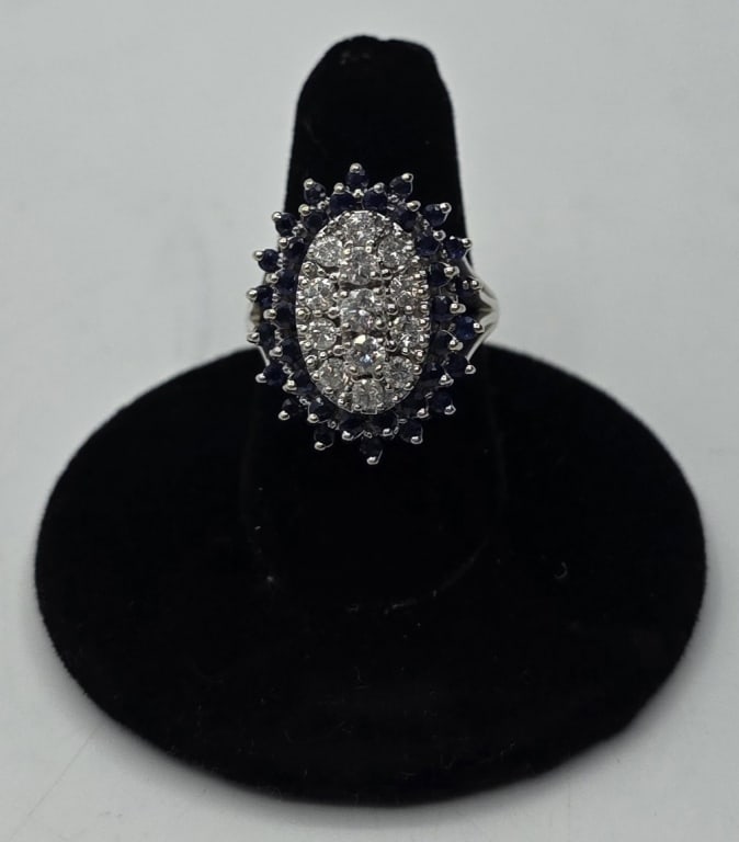 14k Diamond and Sapphire Ring - 8.95g TW: 14k Diamond and Sapphire cocktail ring. 8.95g TW. 13 Prong set round cut center diamonds surrounded by 2 rows of round cut sapphires. All set in 14k white gold. Size 7.5. Approx. 1"H x .75"W. Photos a
