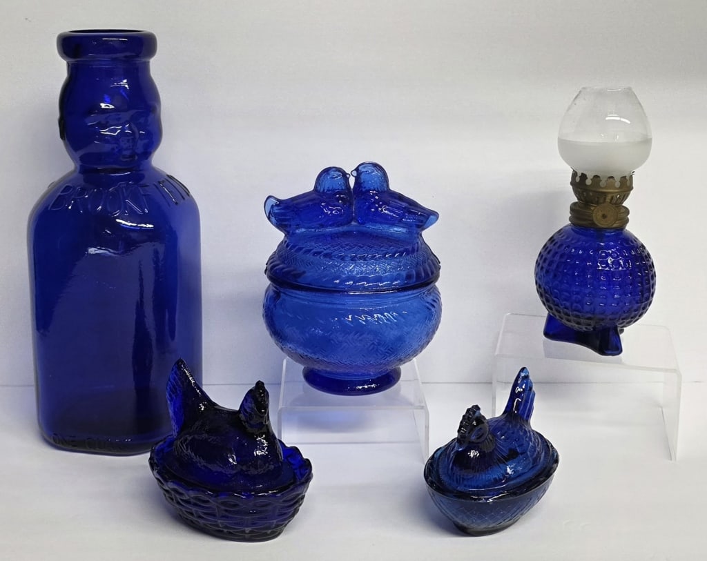 Assorted Vintage Cobalt Blue Glass Collectibles: Collection of assorted vintage cobalt blue glass collectibles. Includes Brookfield "Baby Face" milk bottle, Westmoreland "Kissing Love Birds" dish, miniature hobnail oil lamp, and pair of Hens on Nest