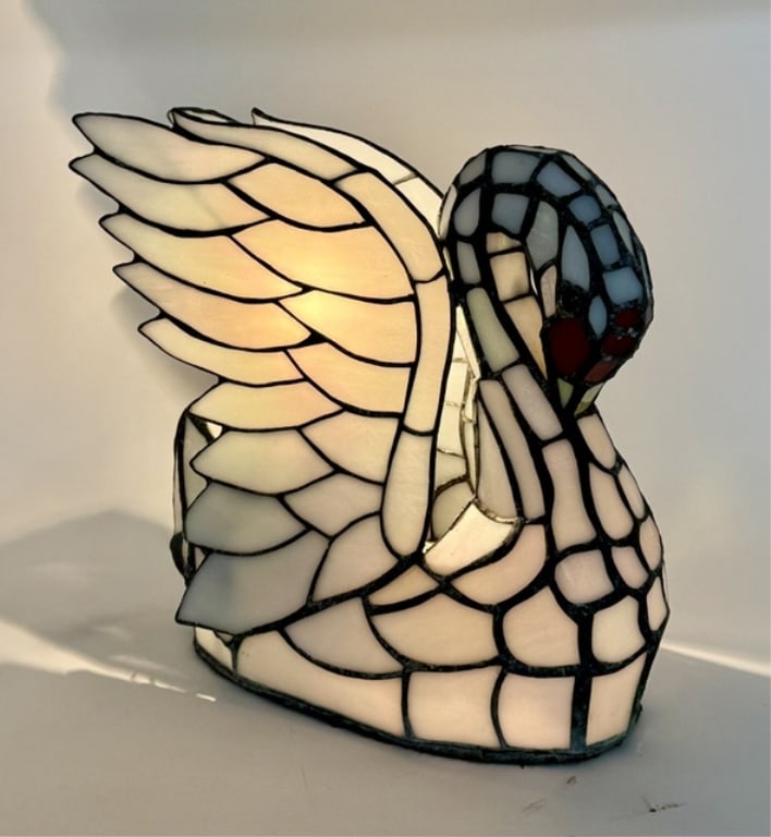 Tiffany Style Swan Table Lamp: Tiffany style swan table lamp. Depicts a detailed swan with a curved neck, red glass eyes, and layered wings that radiate a warm glow when the light bulb inside is turned on. Dual lite. Cord on/off is