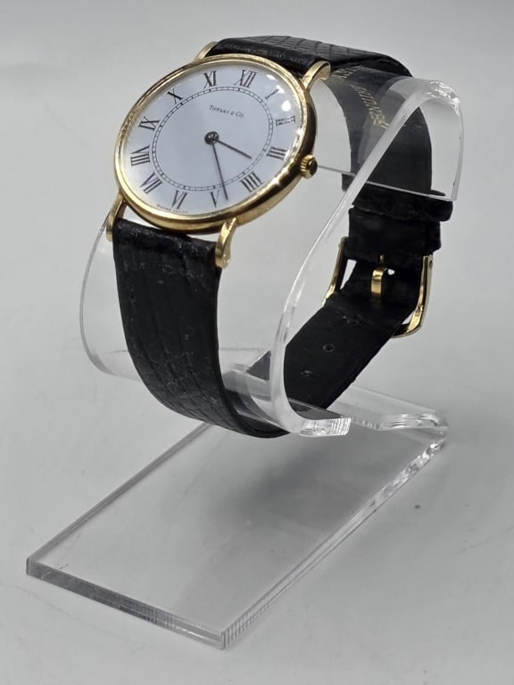 Vintage 14k Tiffany & Co. Watch: Vintage 14k Tiffany & Co. watch. 31mm, 32.2mm with crown included. Classic round white dial quartz watch in yellow gold. Roman numeral hour markers. Watch crown possibly missing gemstone. Some scratch