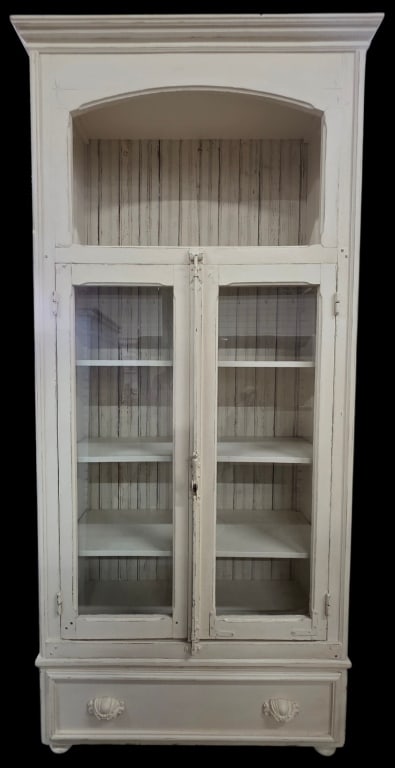 Vintage French Style Glass Front Cupboard: Vintage French style glass front cupboard. Cupboard features a distressed, antique white painted finish, espagnolette latch, and arched open top shelf above two long glass paneled display doors. Singl