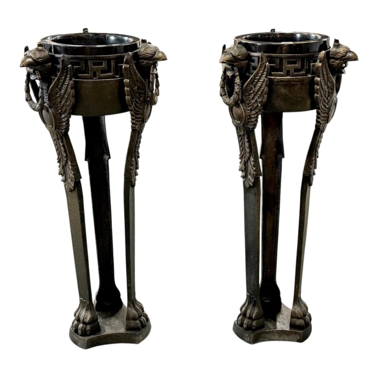Pair Neoclassical Griffin Plant Stands: Pair of Neoclassical griffin plant stands. Foundry iron structure features a classic Greek key pattern background around the upper rim. A trio of winged griffins holding laurel wreaths forms the top s