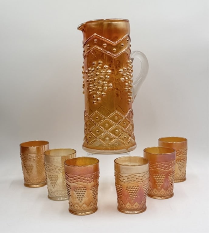 Vintage Marigold Carnival Glass Beverage Set: Vintage marigold carnival glass beverage set. 7 Piece set features "Lattice and Grapes" pattern in a marigold finish with iridescent sheen. Set includes 12" pitcher and six 4" glasses. Some wear of fi