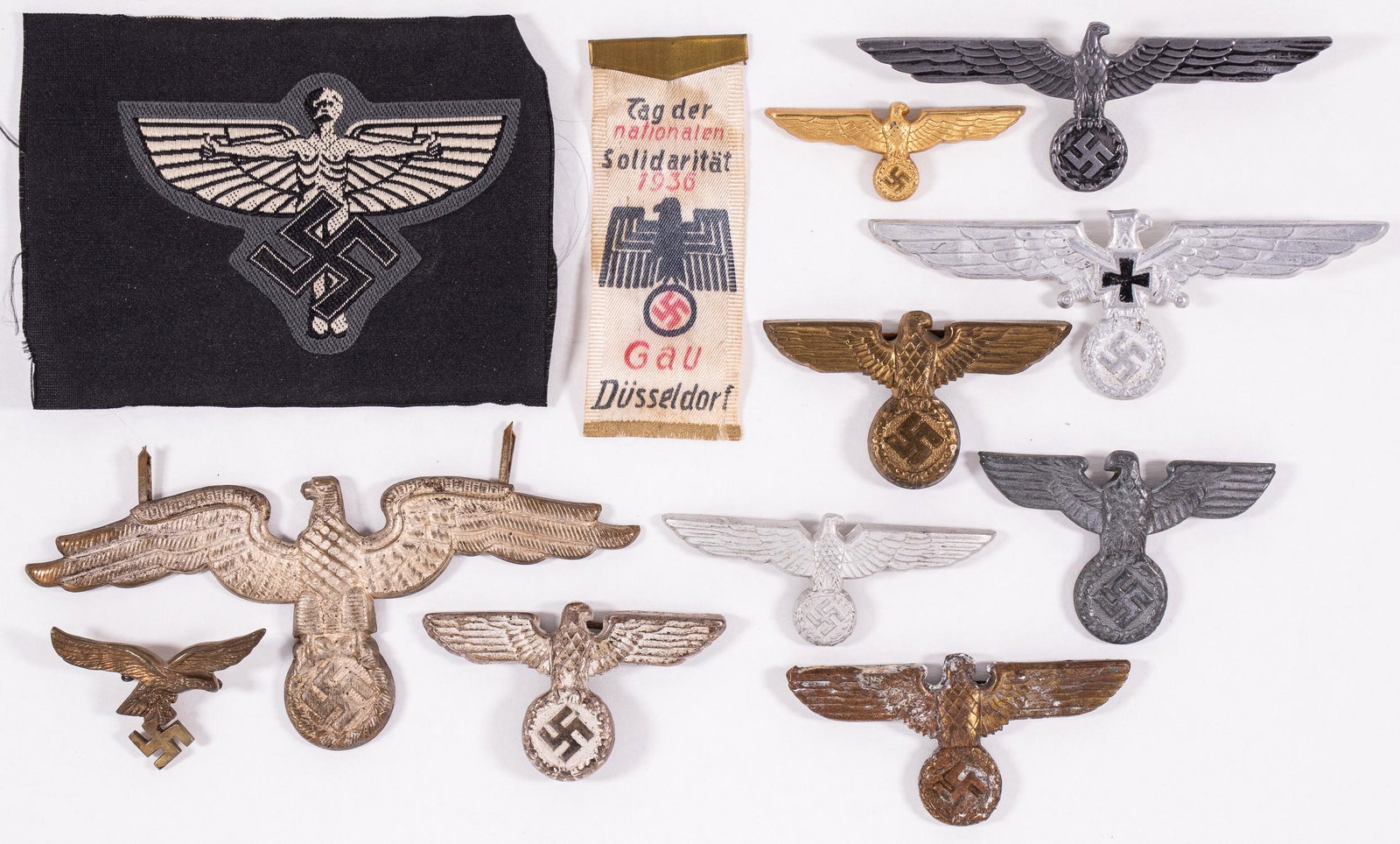 GERMANN WWII EAGLE INSIGNIA AND BADGES (12): Lot of ten German WWII eagle cap badges, pins; one NSFK Glider Korps cloth patch; and a Gau Dusseldorf ribbon for the ''Day of National Solidarity 1936'. Some pins may be missing one or both pins on t
