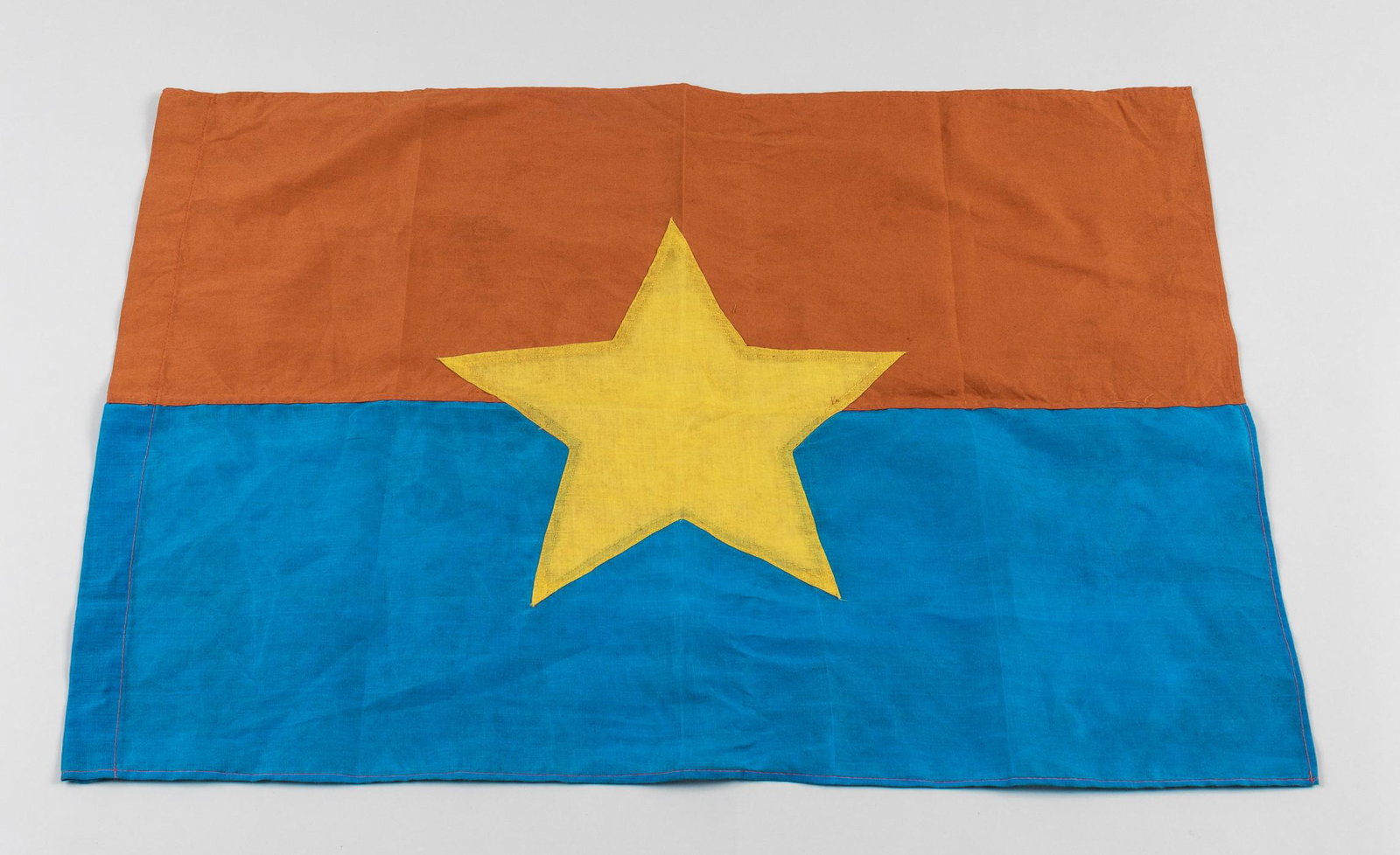 VIET CONG BATTLE FLAG: North Vietnamese army battle flag, 21 x 30 inches, red above light blue, a yellow five-pointed star in the center, three-piece cotton construction.