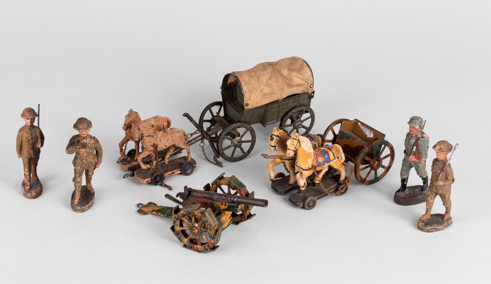 MARKLIN & ELASTOLIN TOYS WWI: Lot of seven WWI toys, including a Marklin WWI toy cannon with a firing mechanism, painted in a camouflage gloss coat; four Elastolin soldiers in varying conditions; a horse-drawn covered wagon; and a