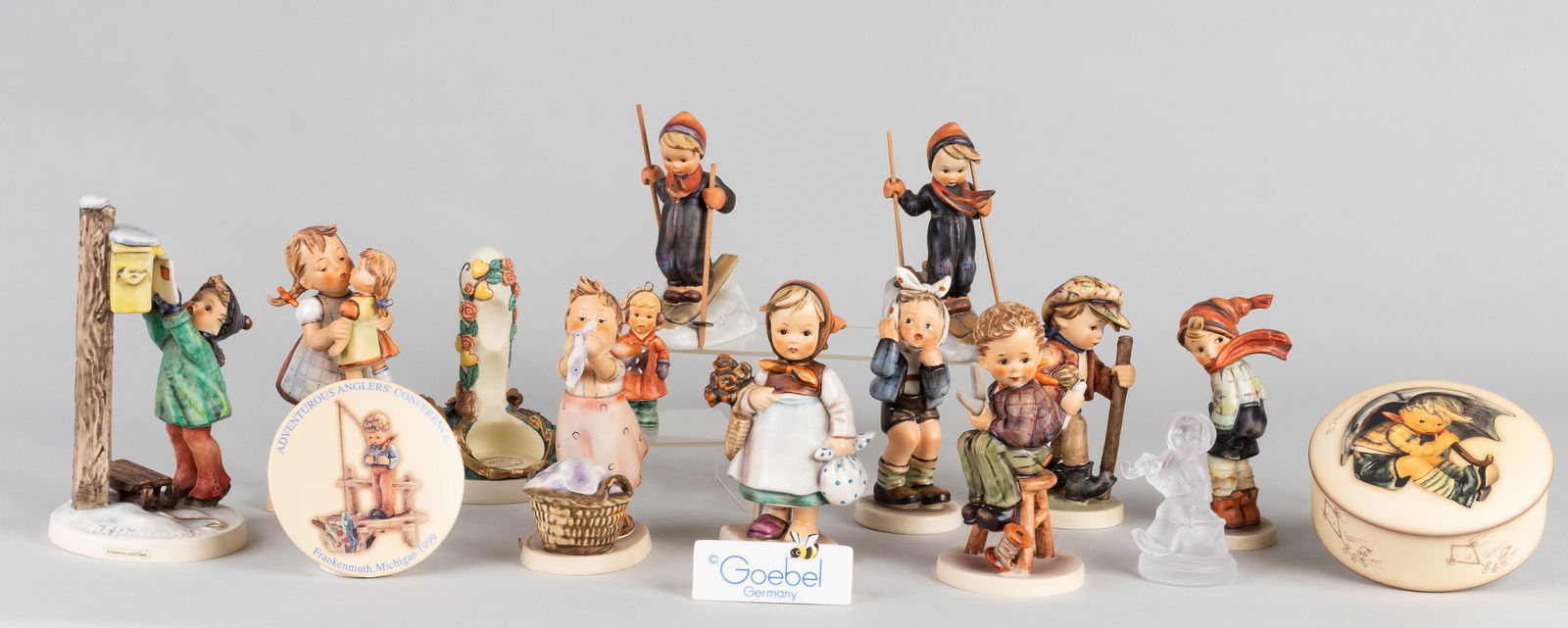 15 GOEBEL HUMMEL FIGURINES: Large lot of fifteen Goebel Hummel figurines, including 'Little Tailor', 'Washday', 'A Letter to Santa Claus', 'On Secret Path', and others. One figurine is broken, repaired with adhesive.