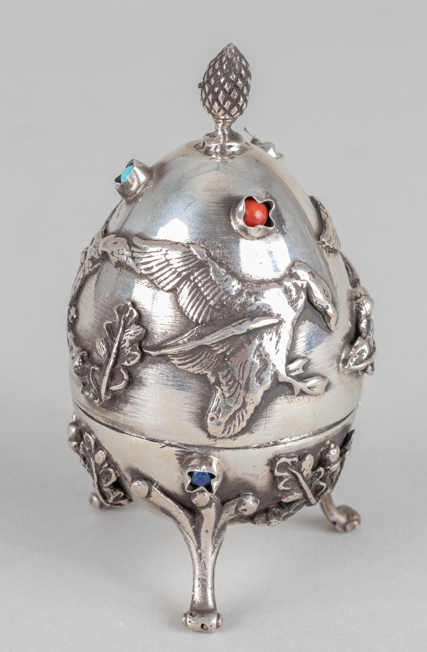 RUSSIAN SILVER HUNTING EGG: Russian silver hunting egg. The egg is adorned with a pinecone. There are a total of six gemstones on the top and bottom of the egg. on the egg, one light blue stone, two dark blue stones, and three r