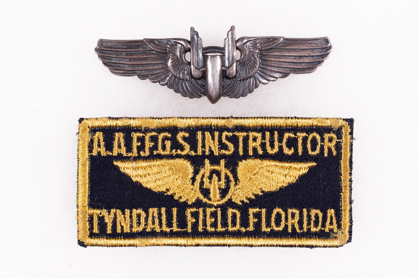WWII AMERICAN A.A.F.F.G.S INSTRUCTOR PATCH AND WINGS: WWII American A.A.F.F.G.S. (Army Air Forces Flexible Gunnery School) patches and wings. The patch is for an instructor at Tyndall Field, Florida. 1.5 x 3.25 inches. The image in the center of the wing