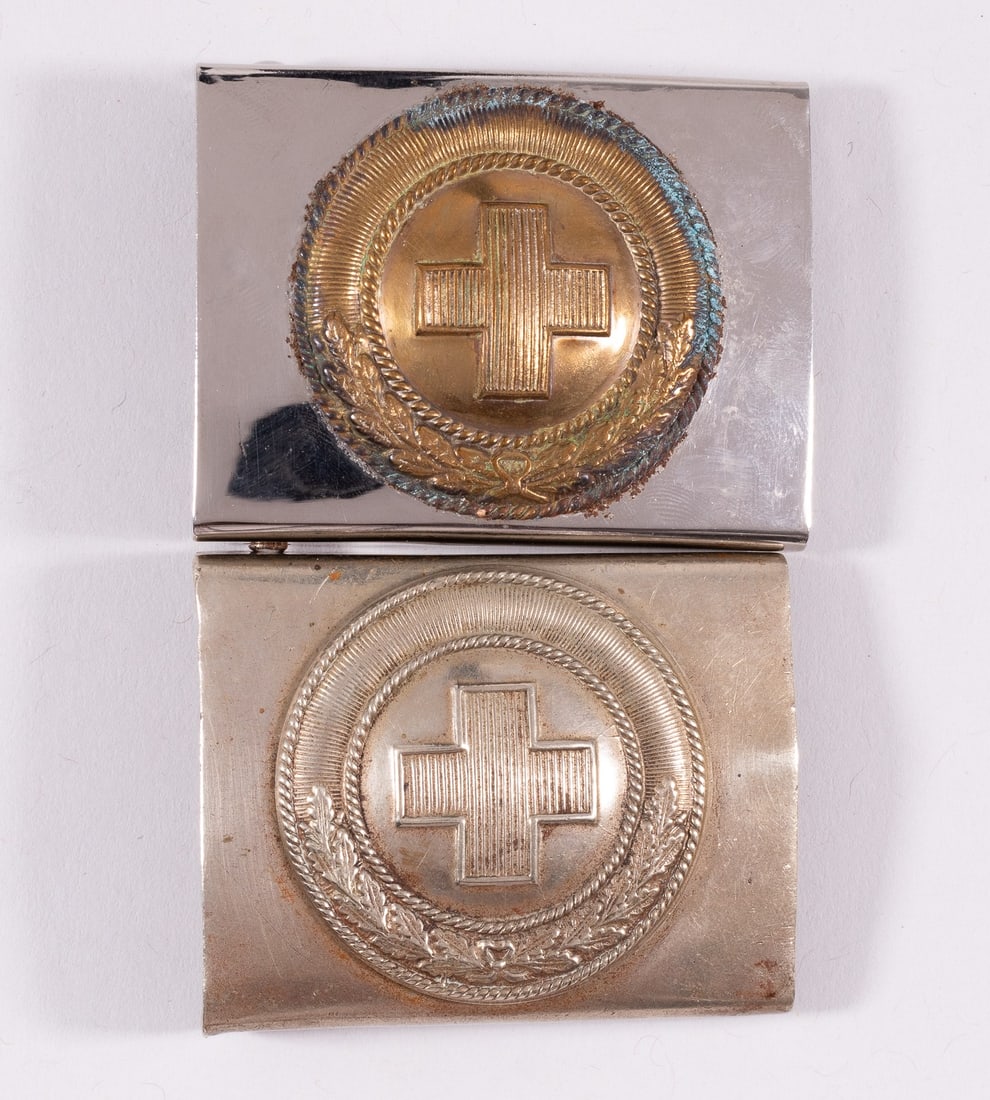 2 GERMAN RED CROSS BELT BUCKLES: Two German Red Cross belt buckles. Both feature the universal logo of the Red Cross in the Center with a half wreath pattern below. One features a brass insignia affixed to the nickel plate, corrosion