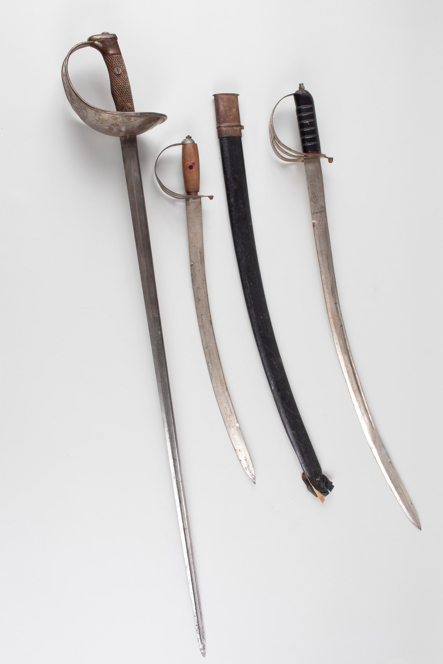 3 CUTLASS STYLE SWORDS: Three cutlass-style swords. One sword features a design with a cross and a crown above on the cupped guard. Average length approximately 34 inches.