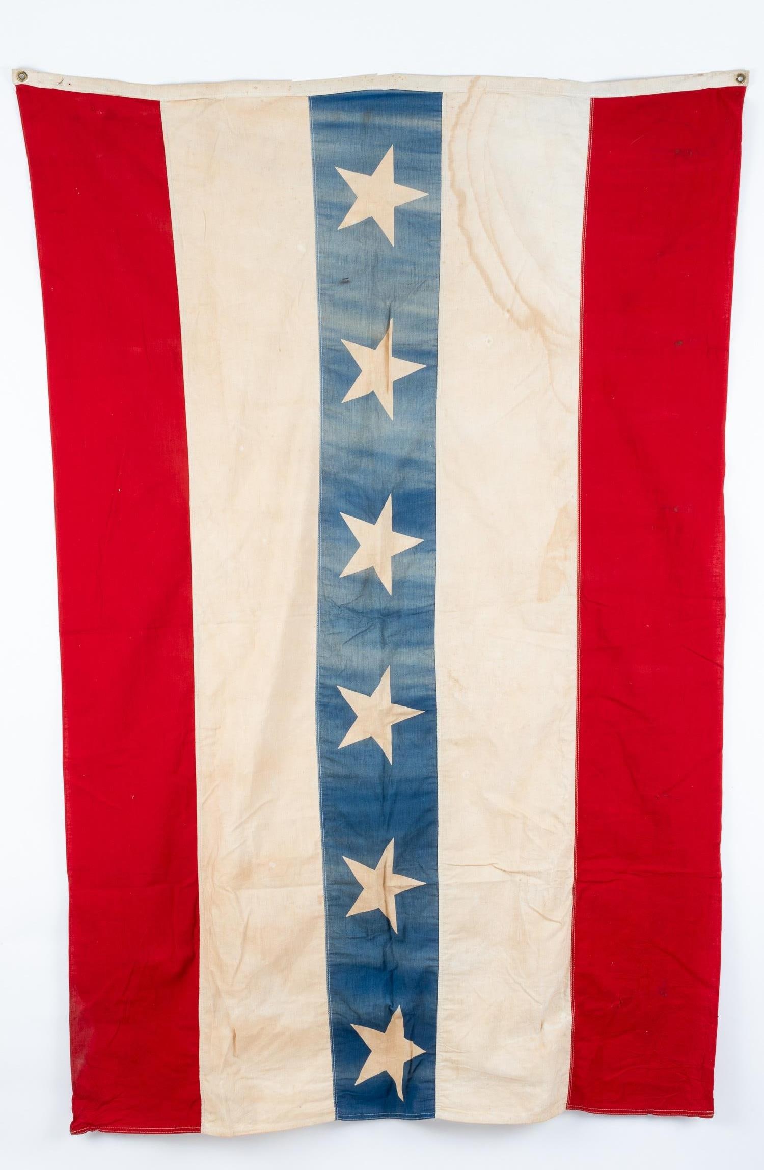 AMERICAN PATRIOTIC VINTAGE FLAG: Vintage American patriotic flag with six stars inside of a blue stripe down the middle, white stripes on either side of the blue stripe, and res stripes on the outside. The flag had two metal rings on