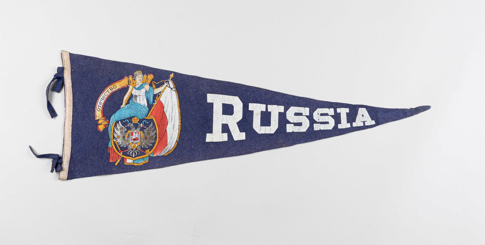 AMERICAN VINTAGE RUSSIA PENNANT: American vintage single-sided pennant with 'Russia' down the length of the fabric. To the left of 'Russia' is a woman sitting on the Russian crest holding a white and red flag with the word 'Fatherlan