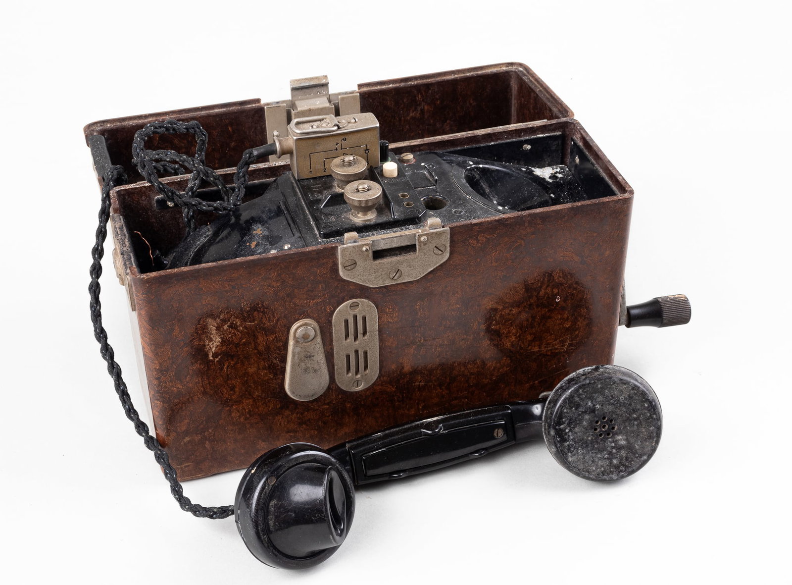 GERMAN WWII FIELD TELEPHONE: A German WWII field telephone. The telephone is in a bakelite box with a crank handle on the right side. The phone sits on a receiver on the inside of the box and on the top of the are diagrams of wir