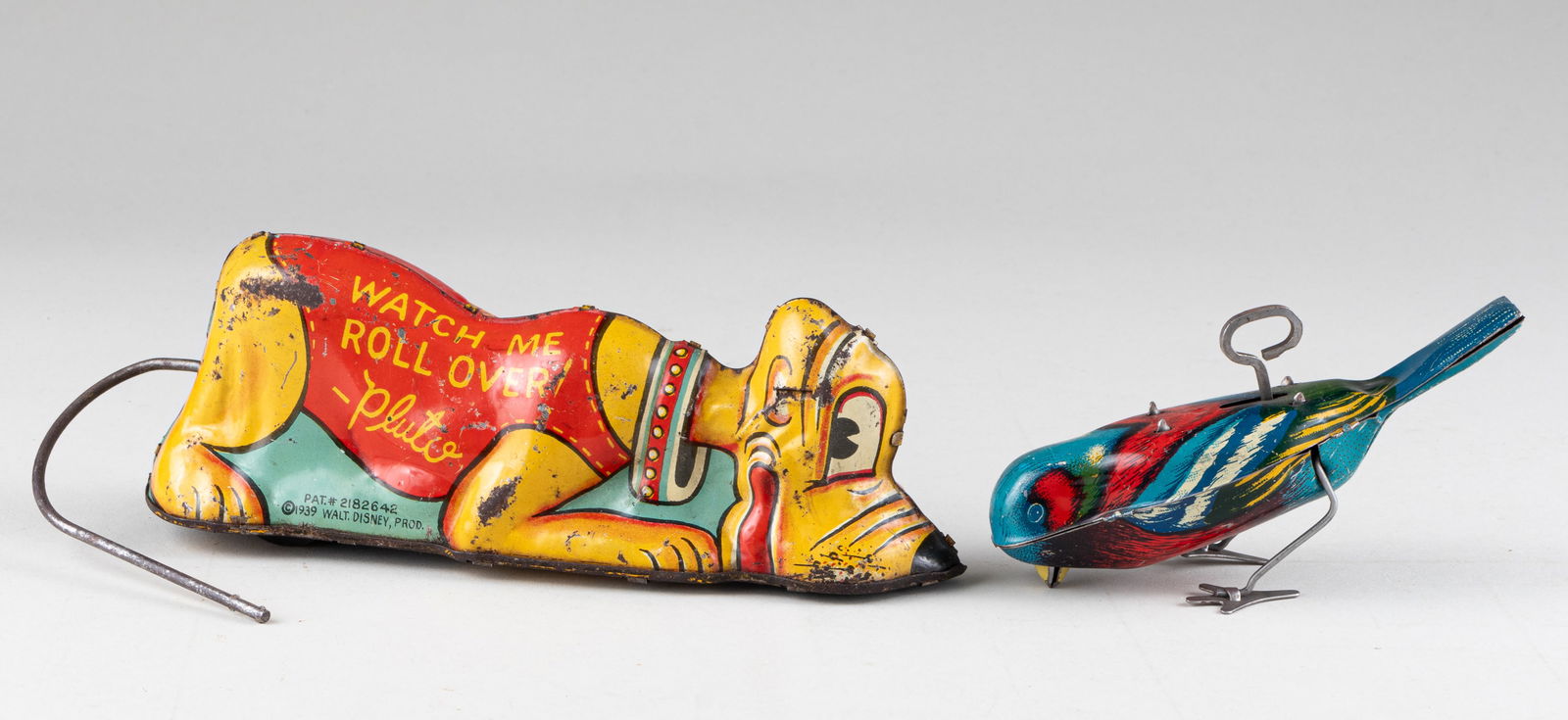 2 TIN TOYS PLUTO BY MARX & BIRD: Wind up Pluto tin toy. 'Watch Me Roll Over - Pluto' created by the Marx company, copyright Walt Disney Prod., 1939. 7.5 inches long. Blue bird wind up tin toy, patented December 27th, 1927. 5 inches l