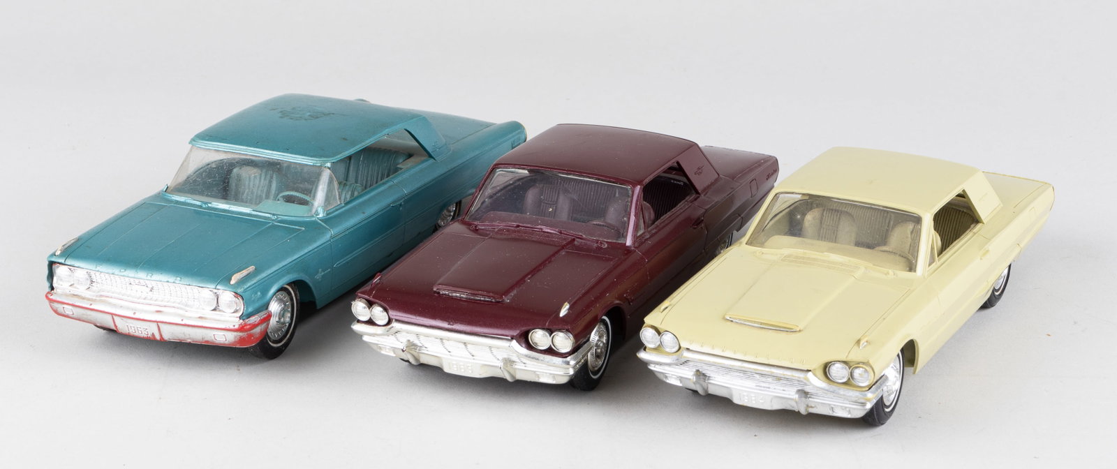 3 1960S FORD PROMOTIONAL CARS: Two promotional cars for the Ford Thunderbird from 1964 and 1965. The 1964 car is in yellow and the 1965 car is in burgundy. On the bottom of the cars is information such as '24,000-mile or 2-year War