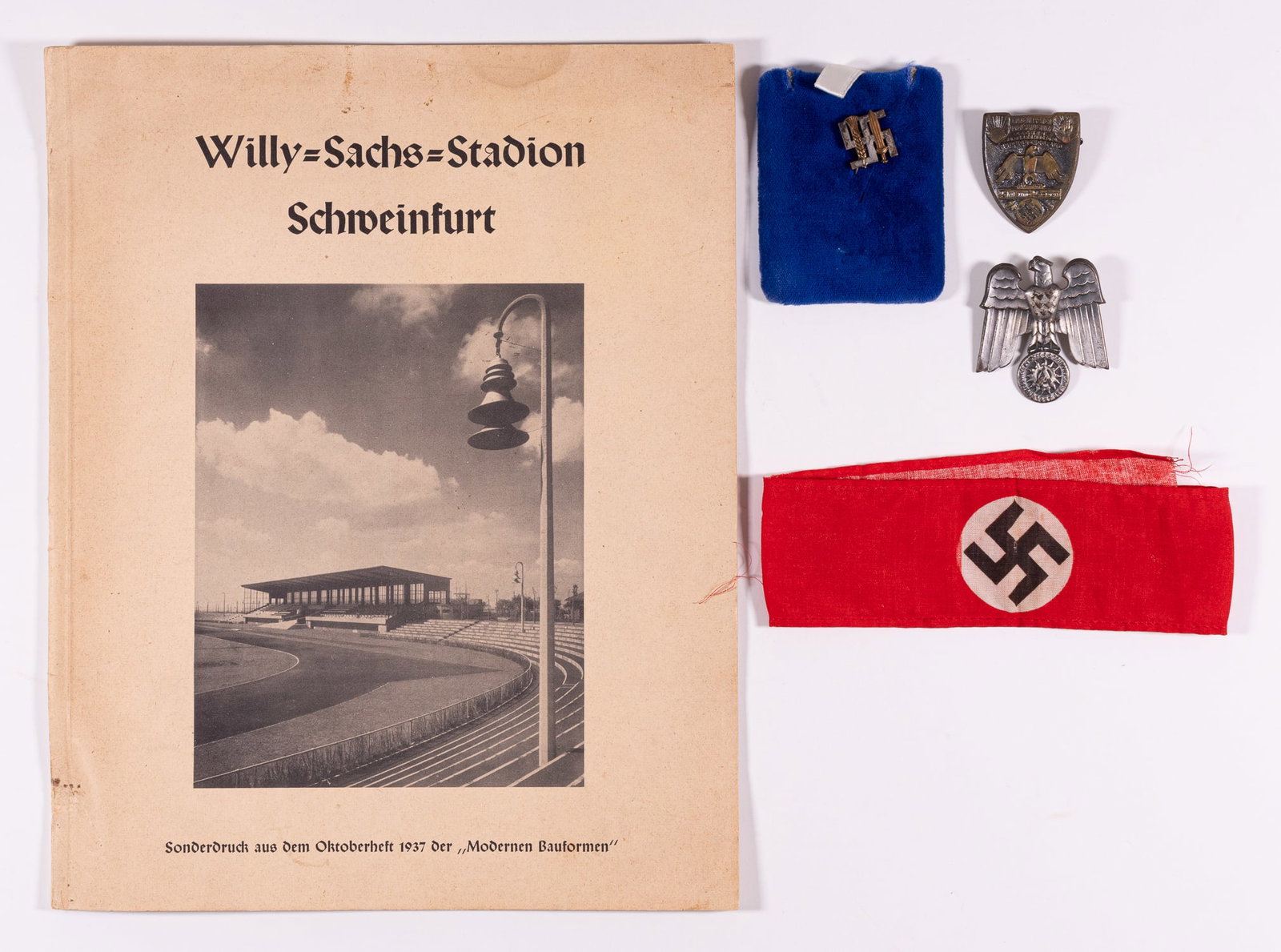 GERMAN WWII TINNIES & ARMBAND: Group of WWII German pins, armband, and a booklet about the Willy Sachs Stadium in Schweinfurt, Germany. The pins include a membership stick pin made by Deschler, Munich, 'Reichsnahrstand - Blut und B