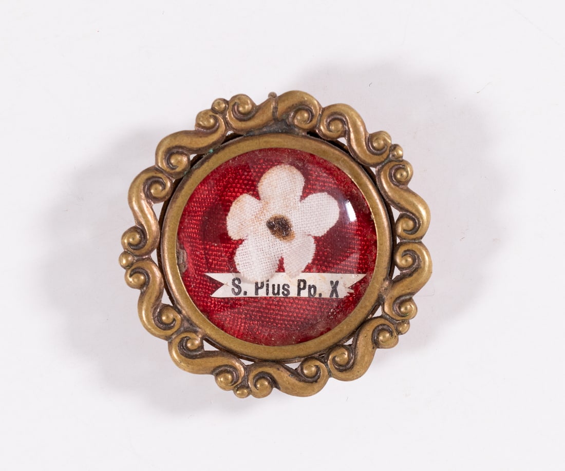 POPE PIUS X FIRST CLASS RELIC: Catholic reliquary relic of Pope Saint Pius X. The relic is housed in round metal theca pendant with handwritten label on red cloth background. Provenance: Acquired from a former priest in Belgium. Th